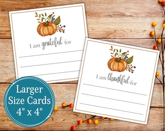 Puede incluir: Dos tarjetas blancas con ilustraciones de calabazas y las frases "Estoy agradecido/a por" y "Estoy agradecido/a por". Las tarjetas miden 10 cm x 10 cm y tienen líneas para escribir.