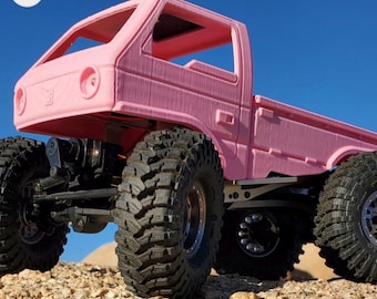 May include: A pink remote-controlled truck with large, black off-road tires. The truck has a detailed cab and bed, and is set against a blue sky and a rocky terrain. The vehicle is designed for rugged outdoor use.