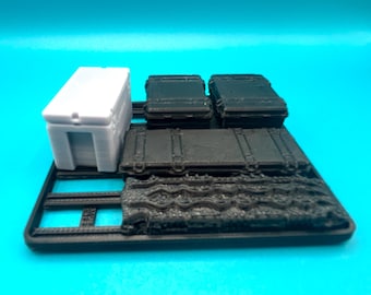 Pode incluir: Uma coleção de pequenos recipientes de armazenamento impressos em 3D em várias formas. Inclui uma caixa retangular branca com uma abertura rebaixada, várias malas pretas e uma base preta texturizada. Os itens estão dispostos em uma plataforma preta.