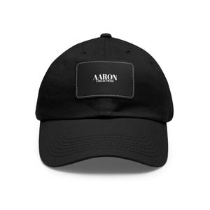以下が含まれることがあります： 白い刺繍の「AARON COLLECTIONS」というパッチが付いた黒いコットン製のベースボールキャップです。