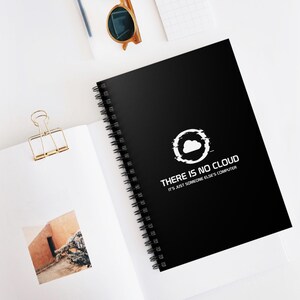 May include: Black spiral-bound notebook with the text "THERE IS NO CLOUD IT'S JUST SOMEONE ELSE'S COMPUTER" and a cloud graphic. The notebook is on a white surface with other office supplies.