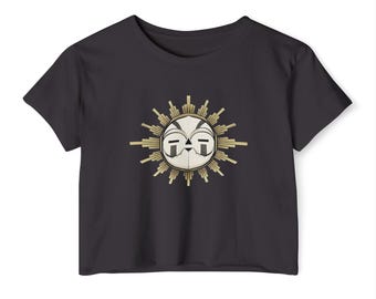 Puede incluir: Un top corto negro con un diseño de sol. El sol tiene una cara blanca con detalles negros y está rodeado de rayos dorados. La camiseta está hecha de un material suave. Es una prenda casual.