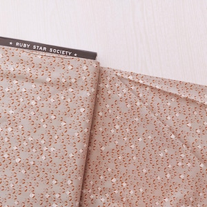 May include: A roll of fabric featuring a repeating pattern of small brown and white shapes on a light grey background. The fabric is labelled "RUBY STAR SOCIETY" in black text on a black background.