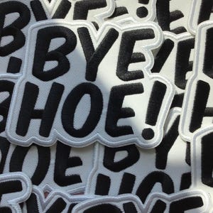 May include: A collection of embroidered fabric patches featuring the black text BYE HOE! on a white background. Each patch has a thick white border and a rounded, irregular shape that follows the contour of the bold, sans-serif lettering.