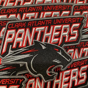 May include: A collection of embroidered patches featuring the text CLARK ATLANTA UNIVERSITY and PANTHERS in red, white, and grey thread. Each patch displays a black panther head silhouette with red and grey accents on a black fabric background.