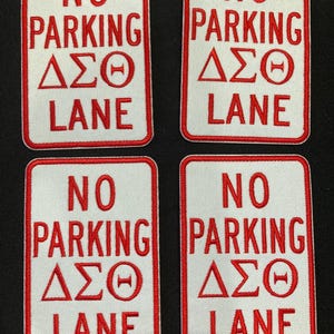 Peut inclure: Quatre écussons rectangulaires brodés avec un fond blanc et une bordure rouge. Chaque écusson présente le texte rouge NO PARKING, les lettres grecques Delta Sigma Theta et le mot LANE, imitant l'apparence d'un panneau de signalisation.