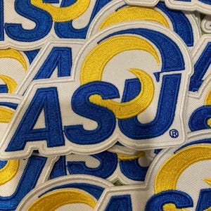 May include: A collection of embroidered patches featuring the letters ASU in blue thread with a yellow crescent shape integrated into the design. Each patch has a white background and a white border, with a small registered trademark symbol.
