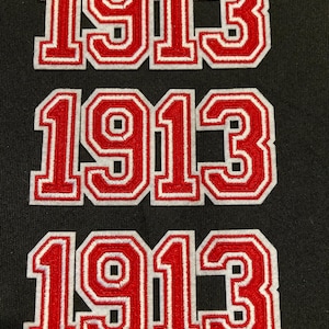 Peut inclure: Trois écussons brodés identiques affichant le nombre 1913 dans une police de style universitaire audacieuse. Chaque écusson présente des chiffres en fil rouge vif avec un contour blanc, créant un contraste net sur le fond sombre.