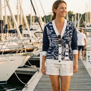 May include: Navy blue cardigan with white trim and a nautical-themed design. The cardigan features a V-neck, button closure, and white illustrations of sailboats, anchors, and marine life. The text "Mer la Vie en Bleu" is also visible.