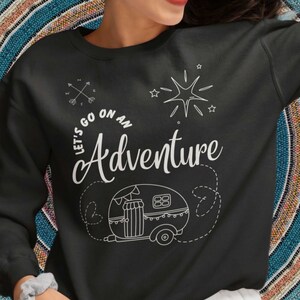 May include: Black sweatshirt with a white graphic design featuring a camper van, a compass, stars, and the text "Let's go on an Adventure".
