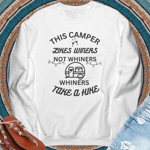May include: White long-sleeved sweatshirt with the text "This Camper Likes Winers Not Whiners Whiners Take a Hike" in black. The text is surrounded by a string of lights and a small camper icon.