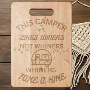 May include: A wooden cutting board with the text "This Camper Likes Winers Not Whiners Whiners Take a Hike" engraved on it. The text is surrounded by a camper trailer graphic and string lights.