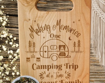 May include: A wooden cutting board with an engraved design of a camper, trees, and the text "Making Memories One Camping Trip at a Time -  Giant Family".