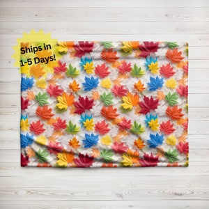 May include: A white fabric blanket with a colorful maple leaf pattern. The leaves are in shades of red, orange, yellow, green, and blue.