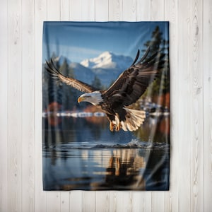 May include: A bald eagle with white head and tail feathers flies over a lake with snow-capped mountains in the background.