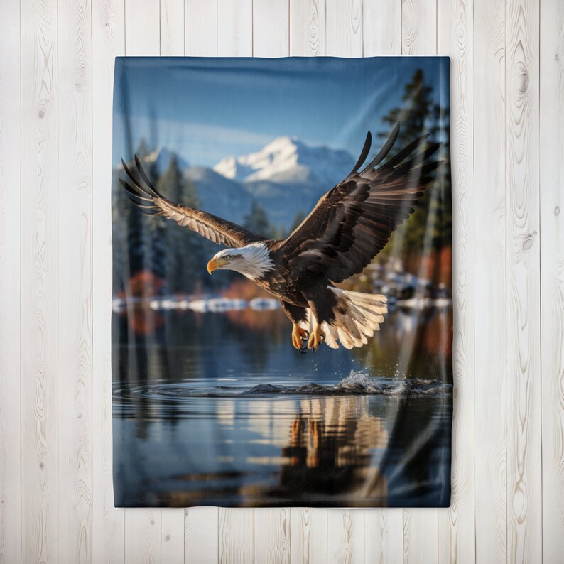 May include: A bald eagle with white head and tail feathers flies over a lake with snow-capped mountains in the background.