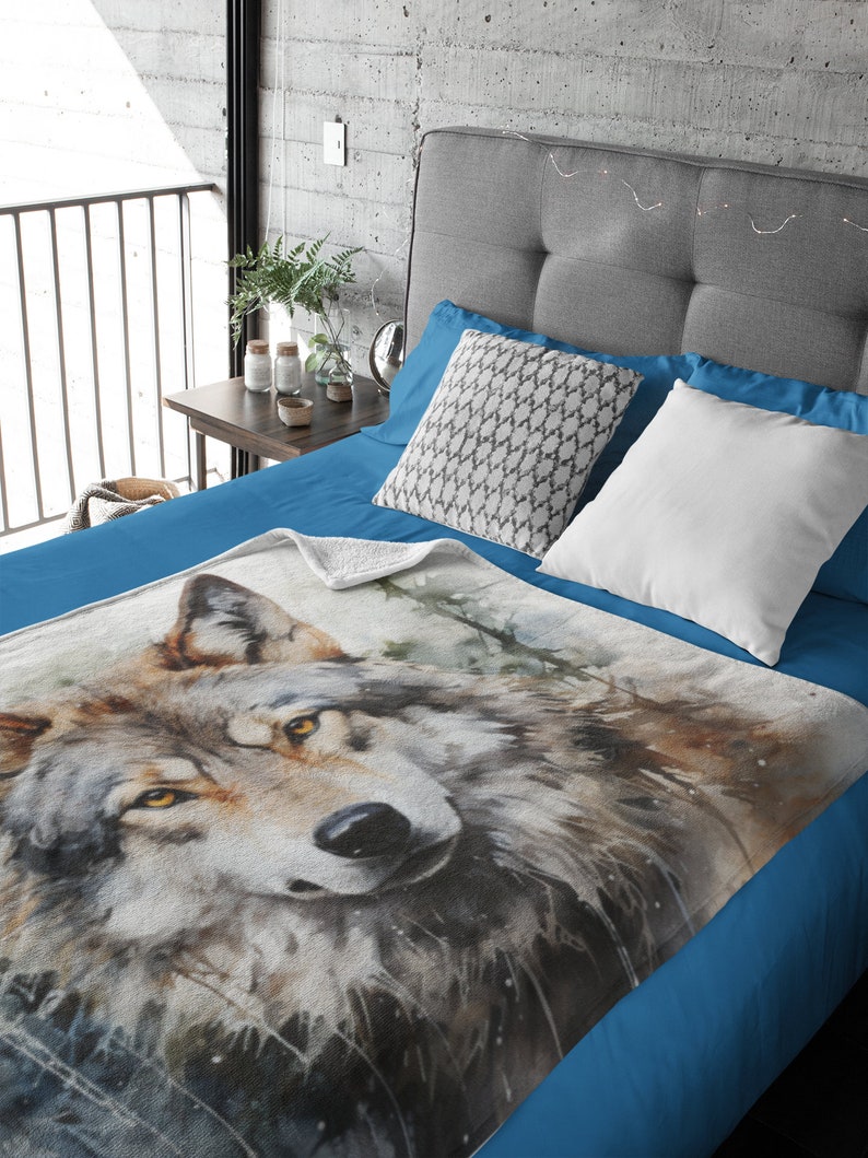 May include: A soft, blue fleece throw blanket with a watercolor painting of a wolf's face. The wolf has brown fur, yellow eyes, and a black nose. The background is a blurry watercolor of trees and leaves.