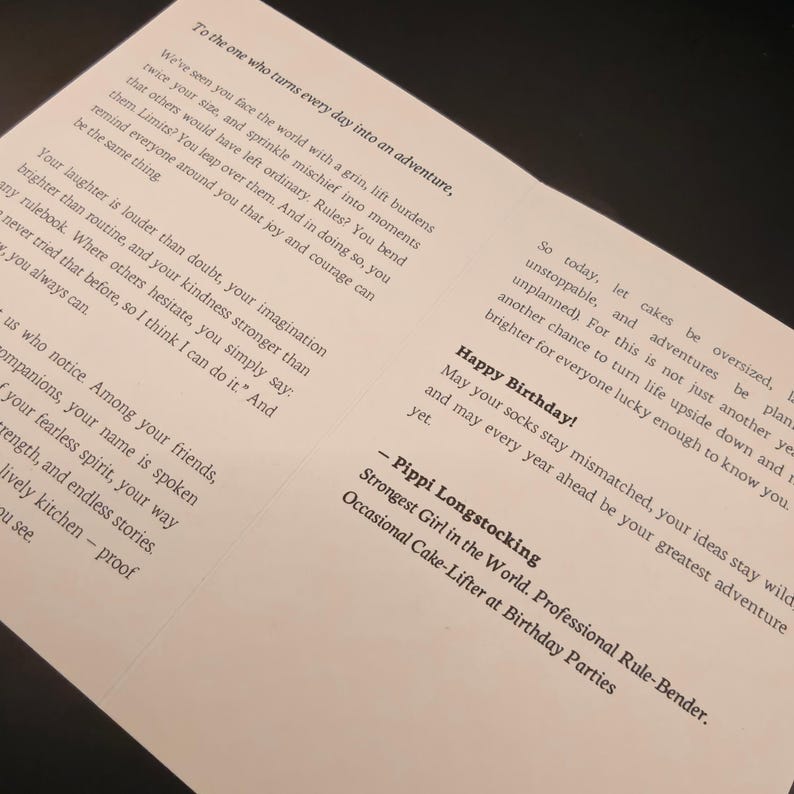May include: A white greeting card with black text. The card's message includes birthday wishes and a quote from Pippi Longstocking. The card is designed to inspire and celebrate life's adventures. The card is on a dark surface.