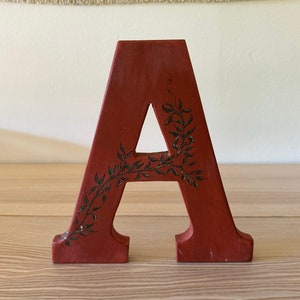May include: A red wooden letter A with a green vine design painted on it.