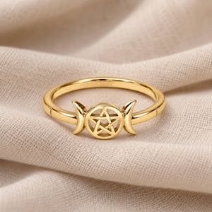 May include: A gold-toned ring featuring a central pentagram symbol flanked by two crescent moon shapes. The band is smooth and circular, with the decorative element integrated into the top section of the metal ring design.