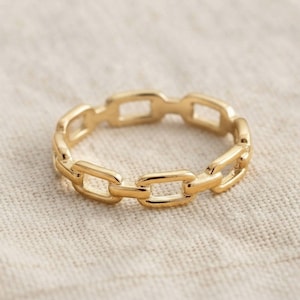 Peut inclure: Une bague dorée présentant un design en maillons de chaîne continus. L'anneau est composé de petits maillons rectangulaires interconnectés aux bords arrondis, créant une apparence métallique uniforme et polie sur toute la structure circulaire.