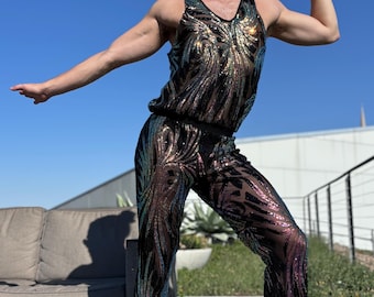 Op de afbeelding: Een persoon draagt een zwarte jumpsuit met pailletten en iriserende accenten. De jumpsuit heeft een mouwloos bovenstuk en een wijde pijp.
