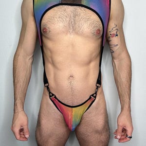 以下が含まれることがあります： 虹色のハーネスとTバックのセット。トップスはメッシュパネルと黒いストラップが特徴です。Tバックは黒い金具でハーネスに接続されています。色は赤から黄色、緑、青へと変化します。