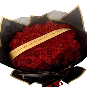 May include: A bouquet of red glitter roses wrapped in black and gold paper. A gold ribbon with the text "I See You For Who You Are. A True Queen" is wrapped around the bouquet. The roses are the focal point of the image.