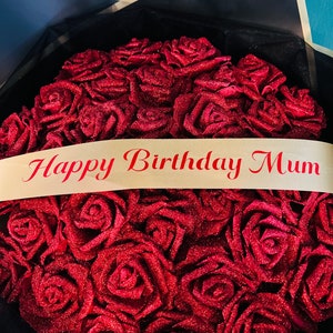 May include: A bouquet of red glitter roses with a cream ribbon that reads "Happy Birthday Mum". The roses are arranged in a circular shape and are wrapped in black paper.