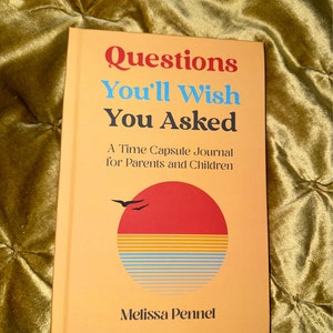 May include: A peach-colored book with the title "Questions You'll Wish You Asked" in red, orange, and black text. The subtitle is "A Time Capsule Journal for Parents and Children" in black text. The cover features a stylized sunset with a red sun, yellow and blue stripes, and two black birds flying above. The author's name, "Melissa Pennel", is printed in black text at the bottom of the cover.