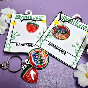 May include: Handmade watermelon-themed jewelry and keychain set. The set includes a pendant with "Viva la Vida" and a watermelon slice design, and a pendant with "Watermelon Sugar". The keychain has a round pendant and a watermelon slice pendant.