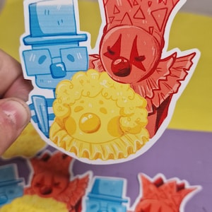 May include: Colorful stickers featuring cartoon clown designs. The stickers showcase a variety of clown characters in red, blue, and yellow. The designs include clown faces, hats, and ruffs, with a playful and whimsical aesthetic.