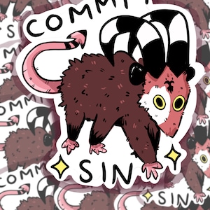 May include: A sticker featuring a cartoon opossum with a pink tail, black and white striped horns, and a red face. The opossum is walking with a sparkle behind it. The text "COMMIT SIN" is written above and below the opossum.
