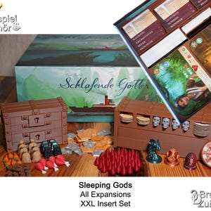 Könnte beinhalten: Eine braune Holzkiste mit Schubladen und Fächern zur Organisation von Spielteilen. Die Kiste ist mit "Schlafende Götter" beschriftet und soll alle Komponenten für das Brettspiel "Sleeping Gods" und seine Erweiterungen aufnehmen. Die Kiste ist Teil eines größeren Sets von Organisatoren für das Spiel.