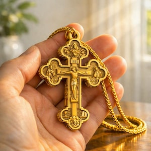 May include: A gold-toned metal crucifix pendant featuring intricate relief carvings of the crucifixion, the letters INRI, and various religious figures. The cross is suspended from a matching gold-toned chain with a woven, textured link design.