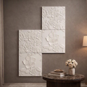 May include: A set of three square white wall panels featuring a raised, three-dimensional floral relief pattern. Each panel displays intricate sculpted flowers and leaves with a matte finish, arranged in a staggered vertical composition on the wall.