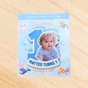 May include: A personalised magnet featuring a child's photo, the number 1, and the words "Happy Birthday." The design incorporates sea creatures and the text "Matteo Turns 1, November 9, 2026."