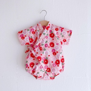 May include: Pink baby onesie with a floral print featuring red and white flowers. The onesie has a kimono style with a wrap-around closure.