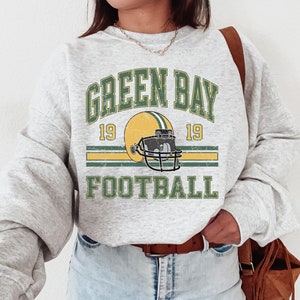 May include: Gray sweatshirt with a vintage-style graphic of a green and yellow football helmet with the text "Green Bay 19 19 Football" printed on it.