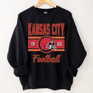 May include: Black sweatshirt with a vintage-style graphic of a football helmet and the text "Kansas City Football" with the numbers 19 and 60 on either side of the helmet.