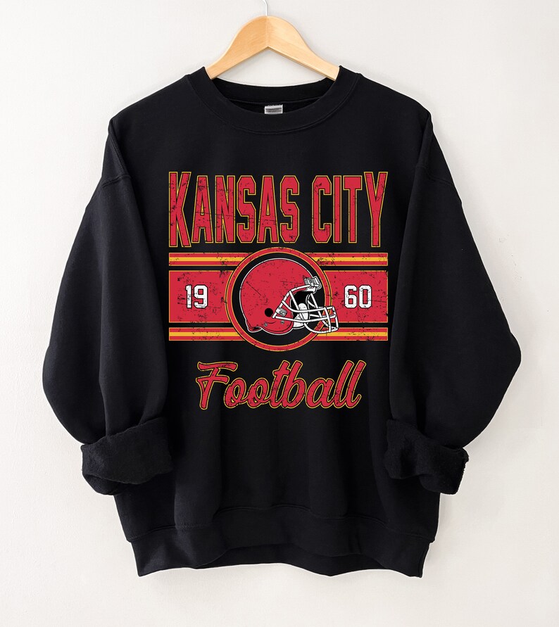 May include: Black sweatshirt with a vintage-style graphic of a football helmet and the text "Kansas City Football" with the numbers 19 and 60 on either side of the helmet.