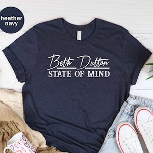 May include: A heather navy blue t-shirt with white text that reads "Beth Dutton State of Mind".