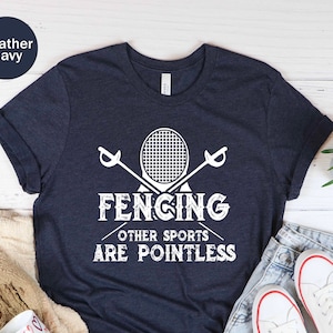 May include: Heather navy t-shirt with a white fencing graphic. The graphic includes crossed swords and a fencing mask, with the text "FENCING OTHER SPORTS ARE POINTLESS". The shirt is paired with denim shorts and white sneakers.