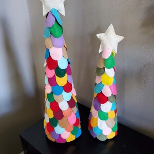 May include: Two colorful felt Christmas trees with white star toppers. The larger tree is decorated with a variety of colors, including red, green, blue, yellow, and pink. The smaller tree is decorated with similar colors, but in a slightly different pattern.