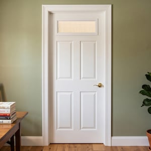May include: A white interior door featuring four rectangular panels and a single horizontal glass window at the top. The door is framed by white molding and includes a polished brass lever handle mounted on the right side of the door panel.