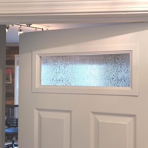 May include: A white interior door with a rectangular frosted glass window. The door is slightly ajar, revealing a glimpse of the room beyond. The door frame is also white.