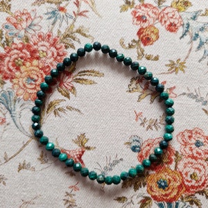 Peut inclure: Un bracelet en pierres précieuses vertes avec des perles facettées. Le bracelet est sur un fond de tissu à motifs floraux.