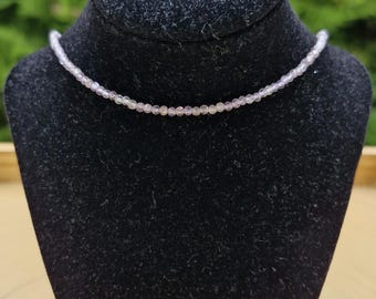 Puede incluir: Un collar delicado hecho de pequeñas cuentas de color púrpura claro. El collar se muestra en un busto de terciopelo negro.