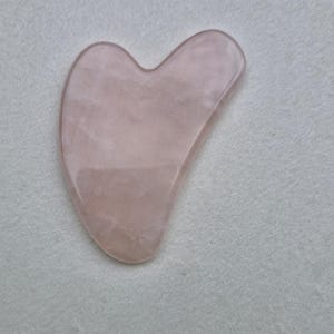 Peut inclure: Un outil de massage facial en forme de cœur en quartz rose. L'outil est lisse et poli, avec une teinte rose clair.