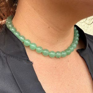 May include: A green jade bead necklace with round beads. The necklace is worn by a person with a black shirt.